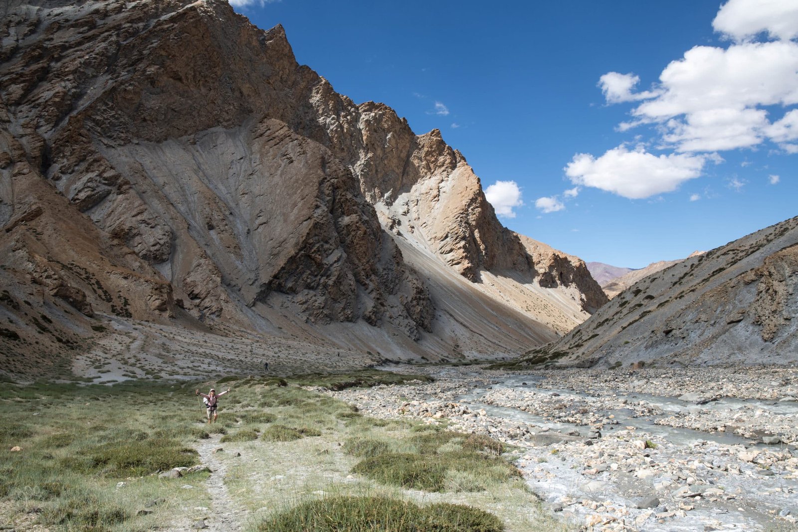 A hiker walks through a rocky mountain valley with a stream in ladakh