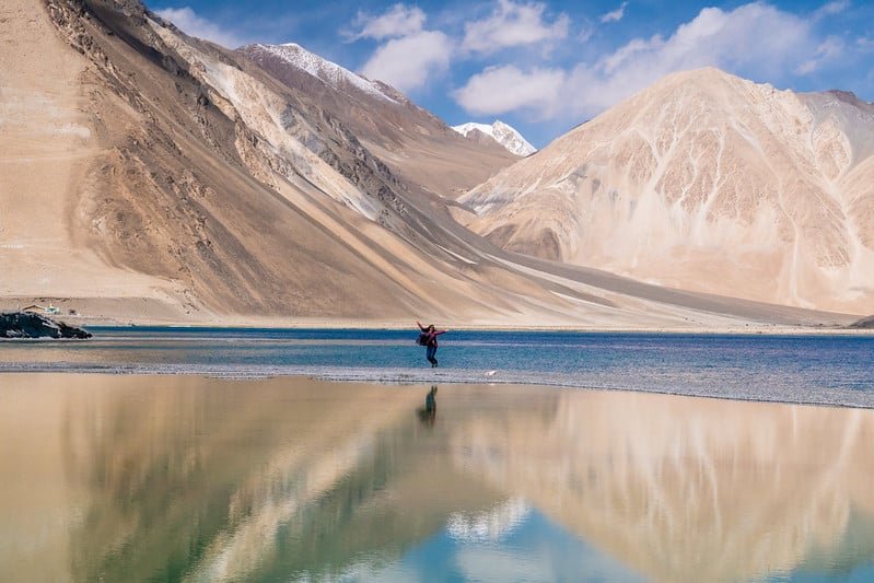 A person stands joyfully at the edge of a stunning blue lake in leh ladakh in august