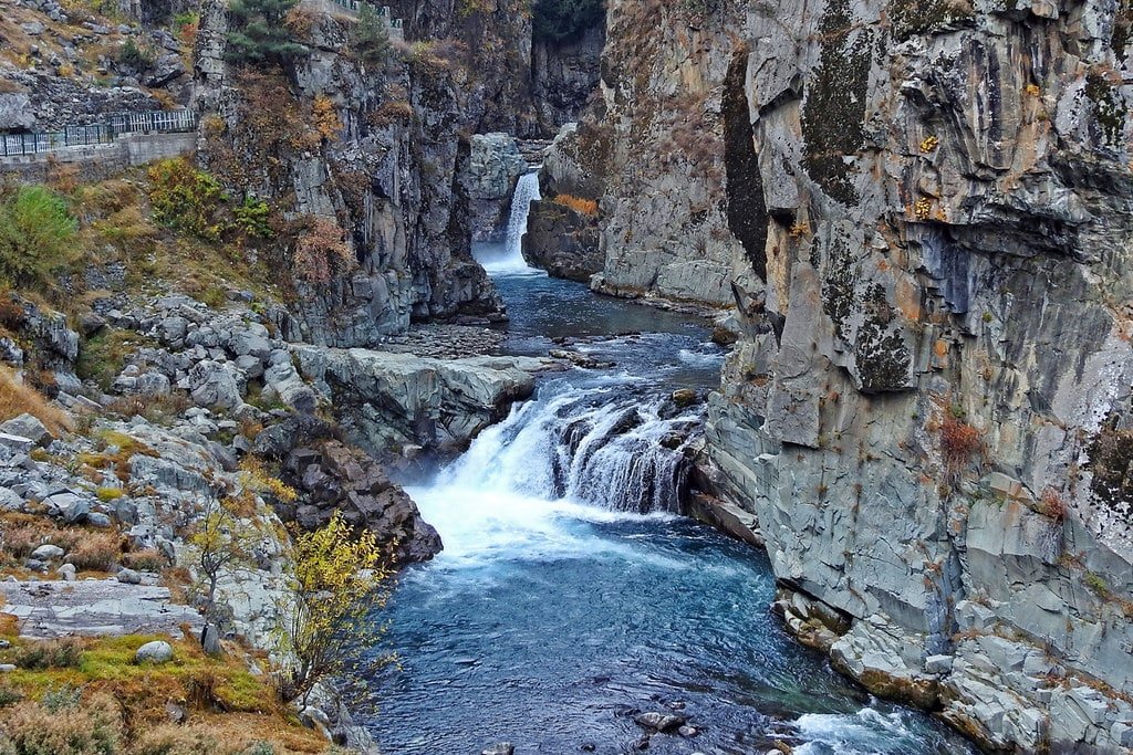 Aharbal Waterfall flowing through rocky cliffs and clear blue water.