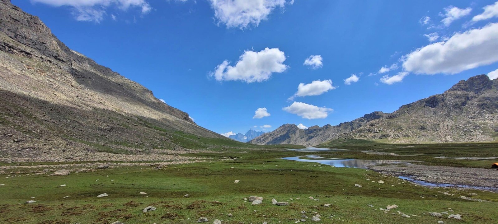 baisaran valley with a stream, green meadows, and a bright blue sky with clouds