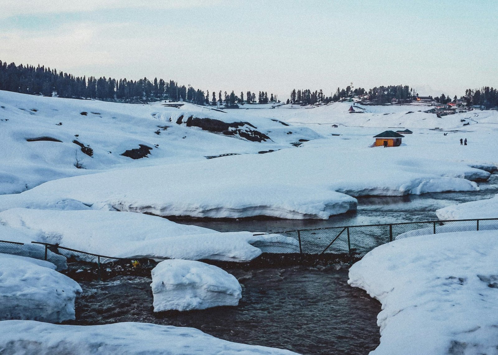 Snow-covered landscape with a stream and a small yellow hut in Kashmir