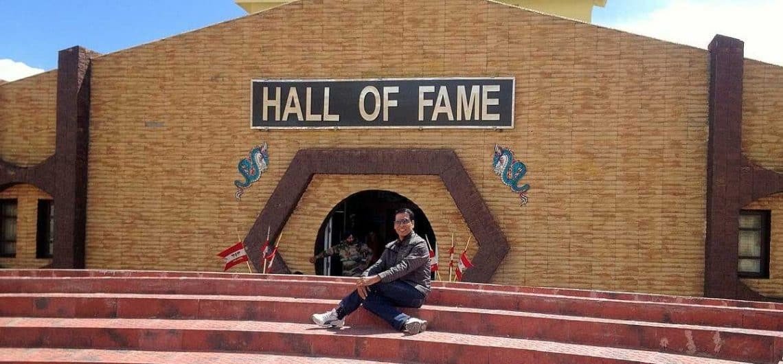 Person sitting on red steps in front of the Hall of Fame building in Leh