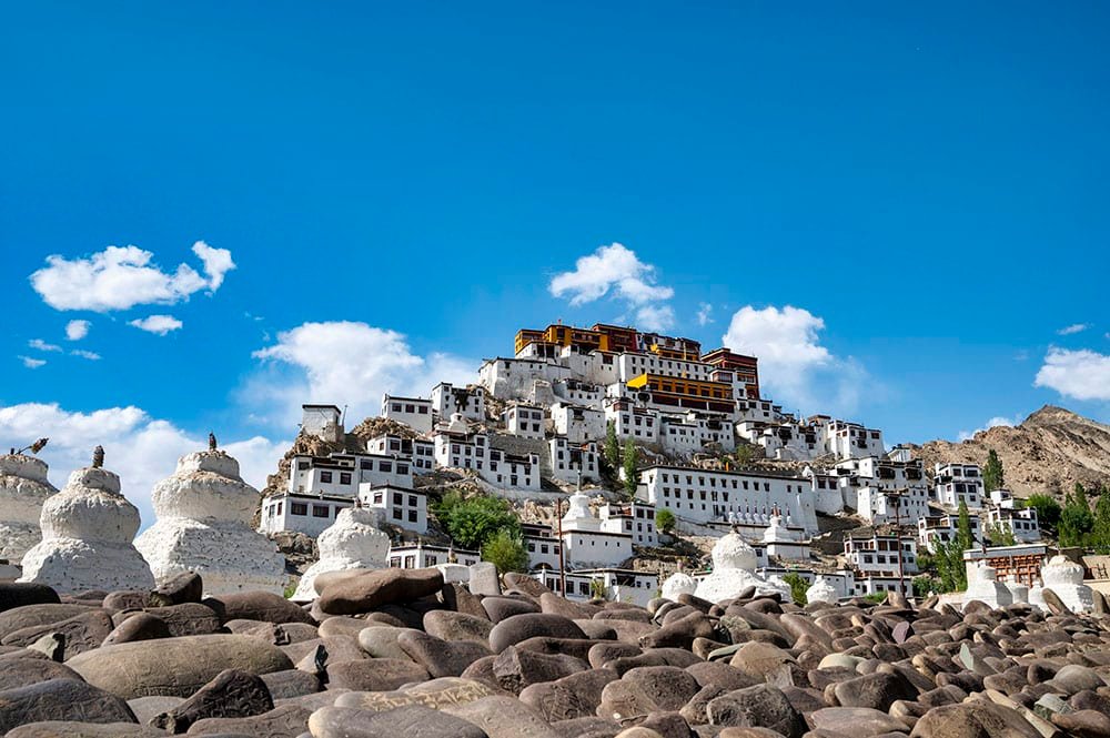 Thiksey Monastery on a hilltop under a blue sky with scattered clouds.