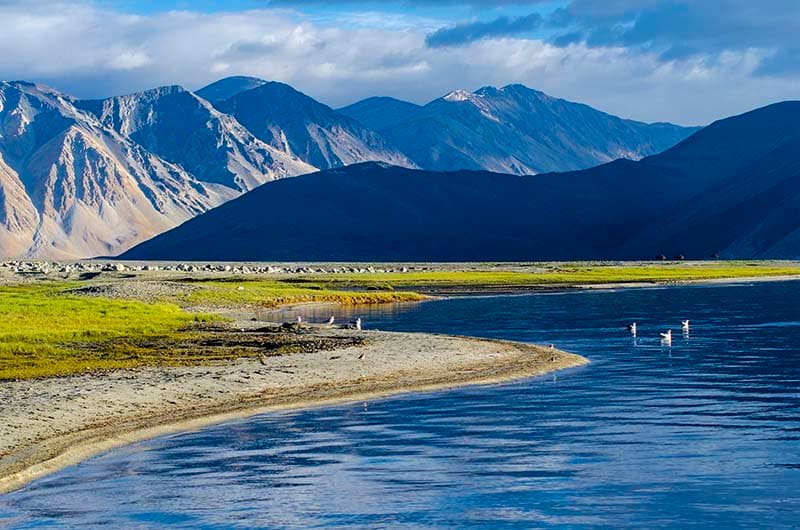 Calm blue waters of Yarab Tso Lake surrounded by green shores and rugged mountains