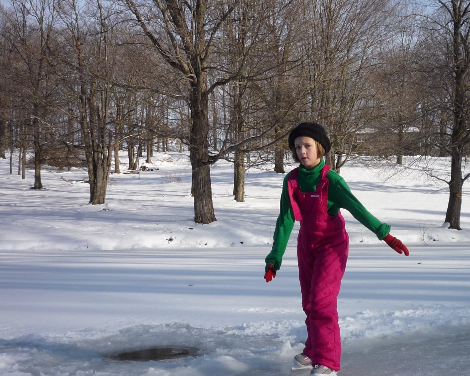 Child ice skating on a frozen pond in a snowy forest.