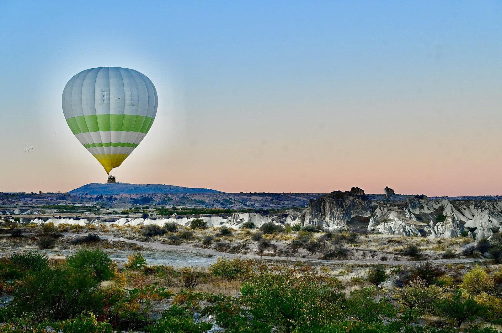 Hot air balloon flying over rocky landscape at sunset