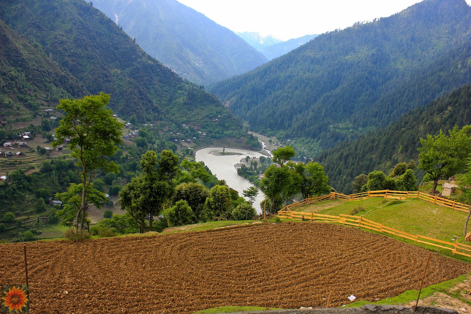 A scenic mountain valley with terraced fields in the foreground, a winding river below, and dense forested hills surrounding small villages.