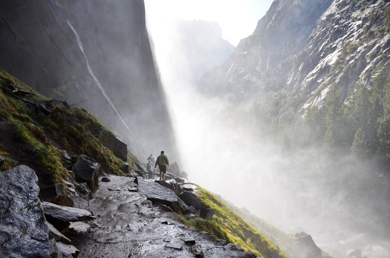 Trekkers walking on a misty mountain trail near a waterfall in chadar trek
