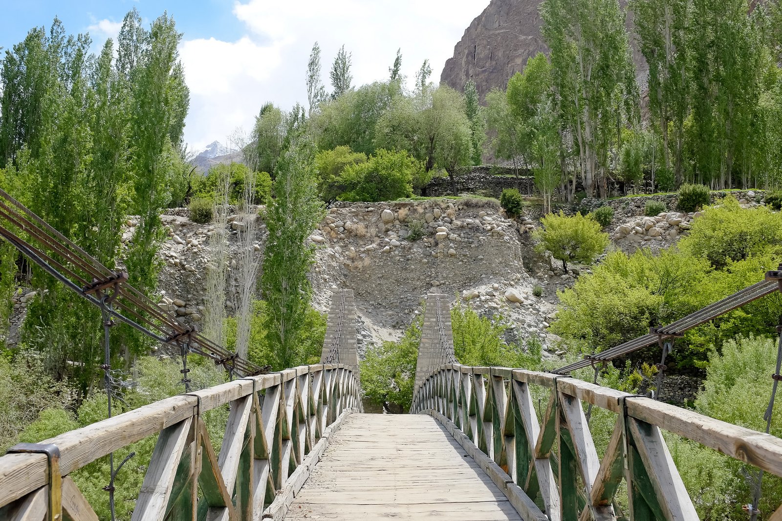 Wooden suspension bridge leading to forested hillside near Balti Heritage House in Turtuk