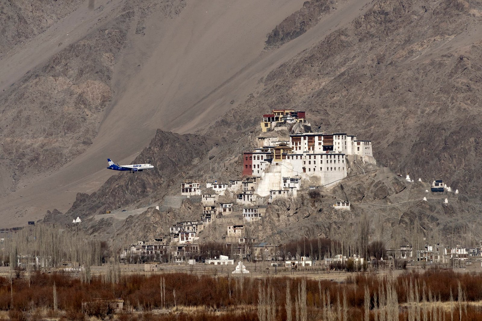 spituk monastery is Hilltop with buildings and a plane flying nearby in a mountain valley