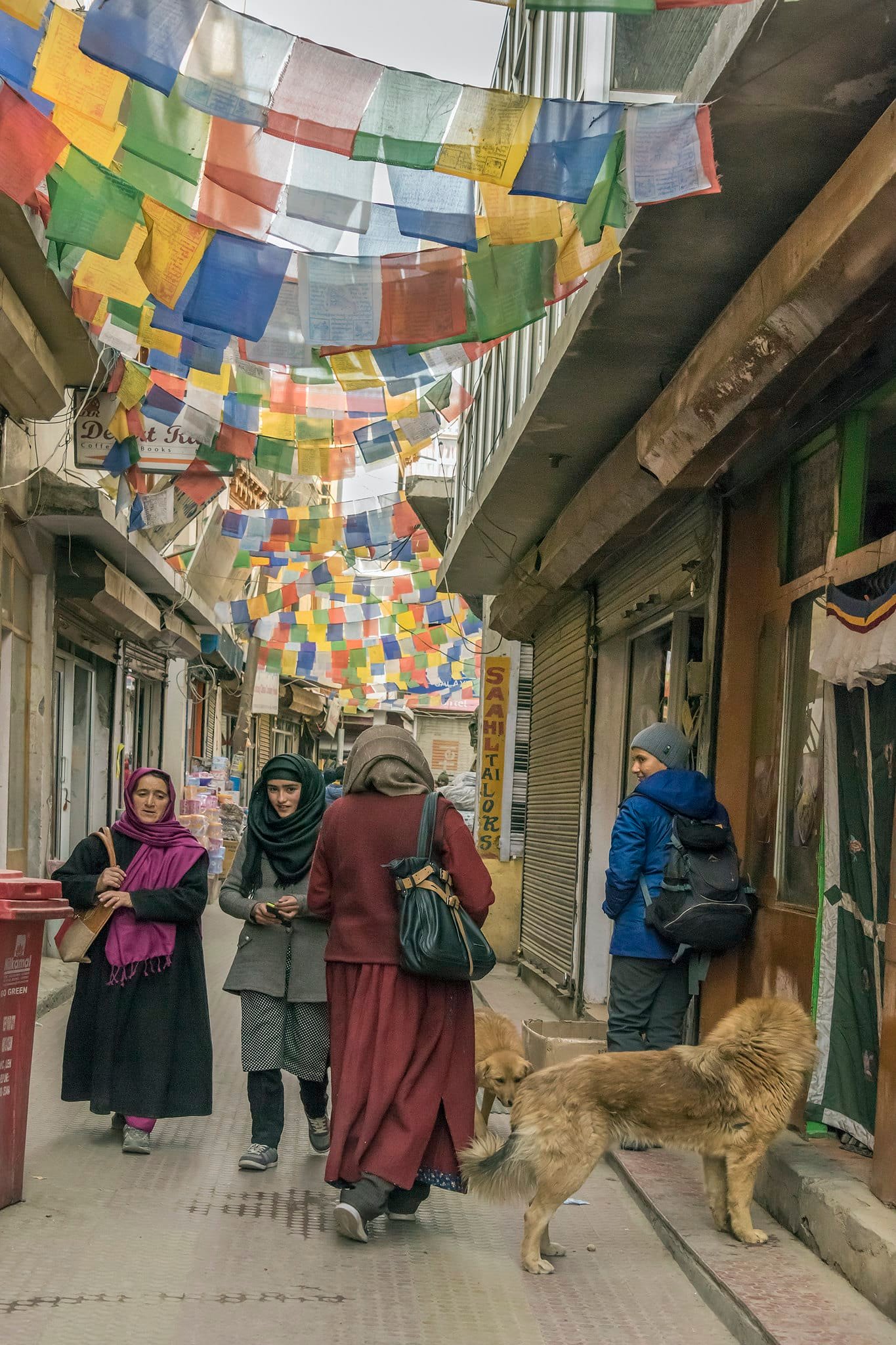 People walking in a colorful market street in Leh decorated with prayer flags