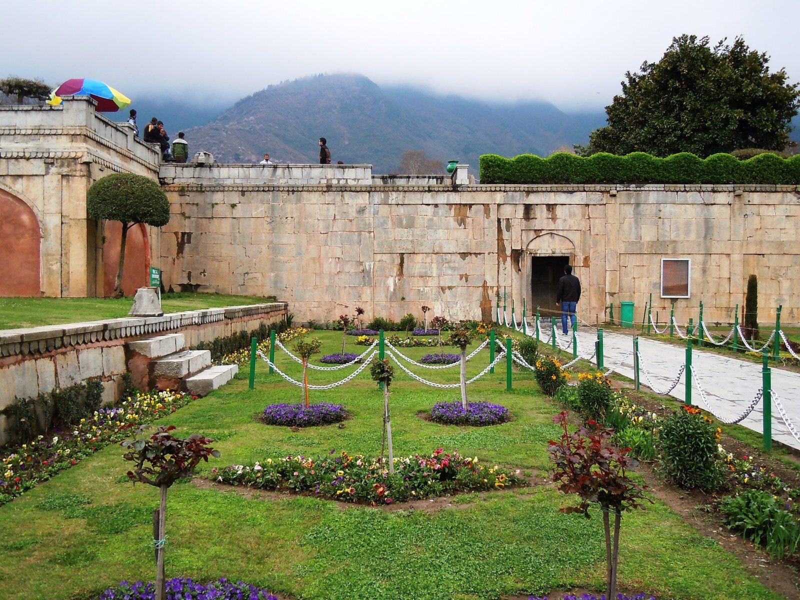 Beautiful nishant garden with colorful flower beds, manicured grass, and a stone pathway leading to an arched entrance in kashmir