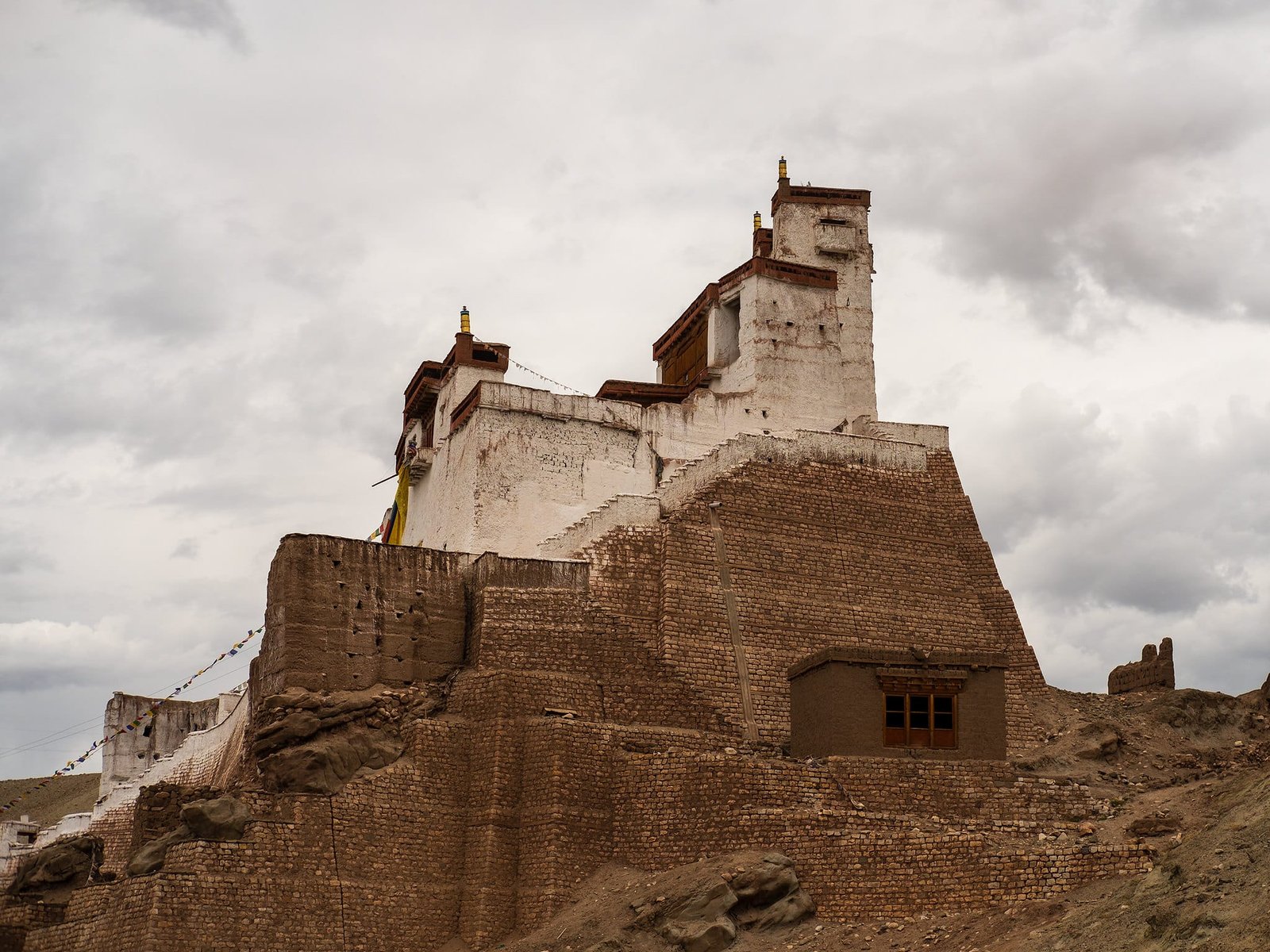 Ancient Basgo Monastery with mud-brick walls set on a rocky hill under a cloudy sky