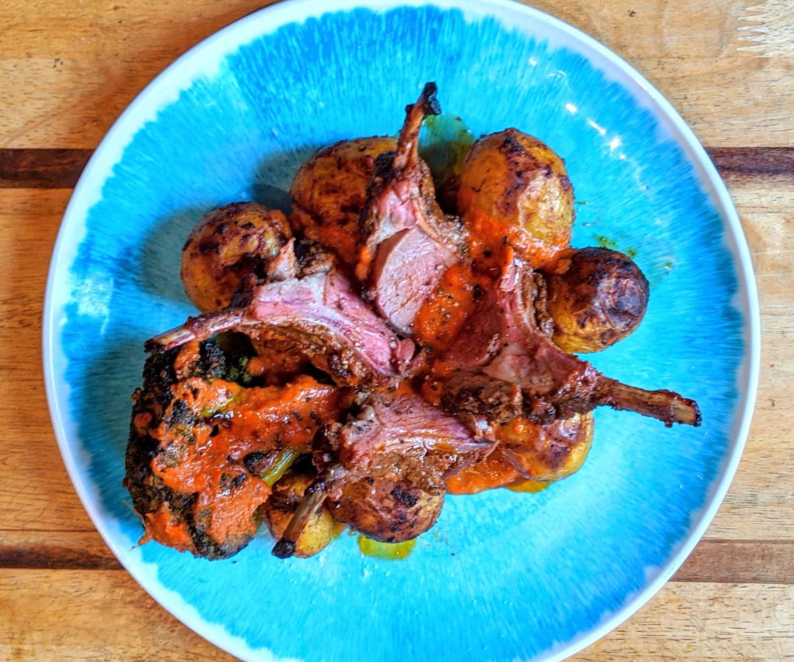 Grilled lamb chops served with roasted baby potatoes and red sauce on a blue plate