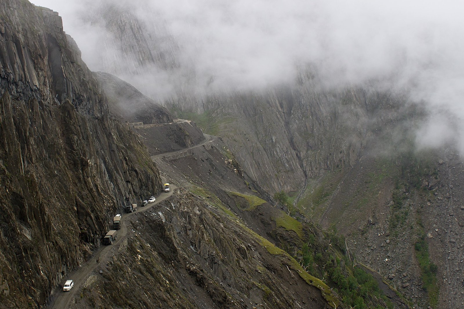 A foggy view of Zoji La Pass, showing a narrow, rugged mountain road carved into steep rocky cliffs