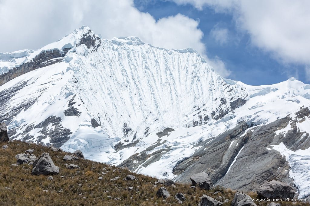 Snow-covered mountain with steep icy ridges under a blue sky, with rocky grassland in the foreground in pahalgam, kashmir