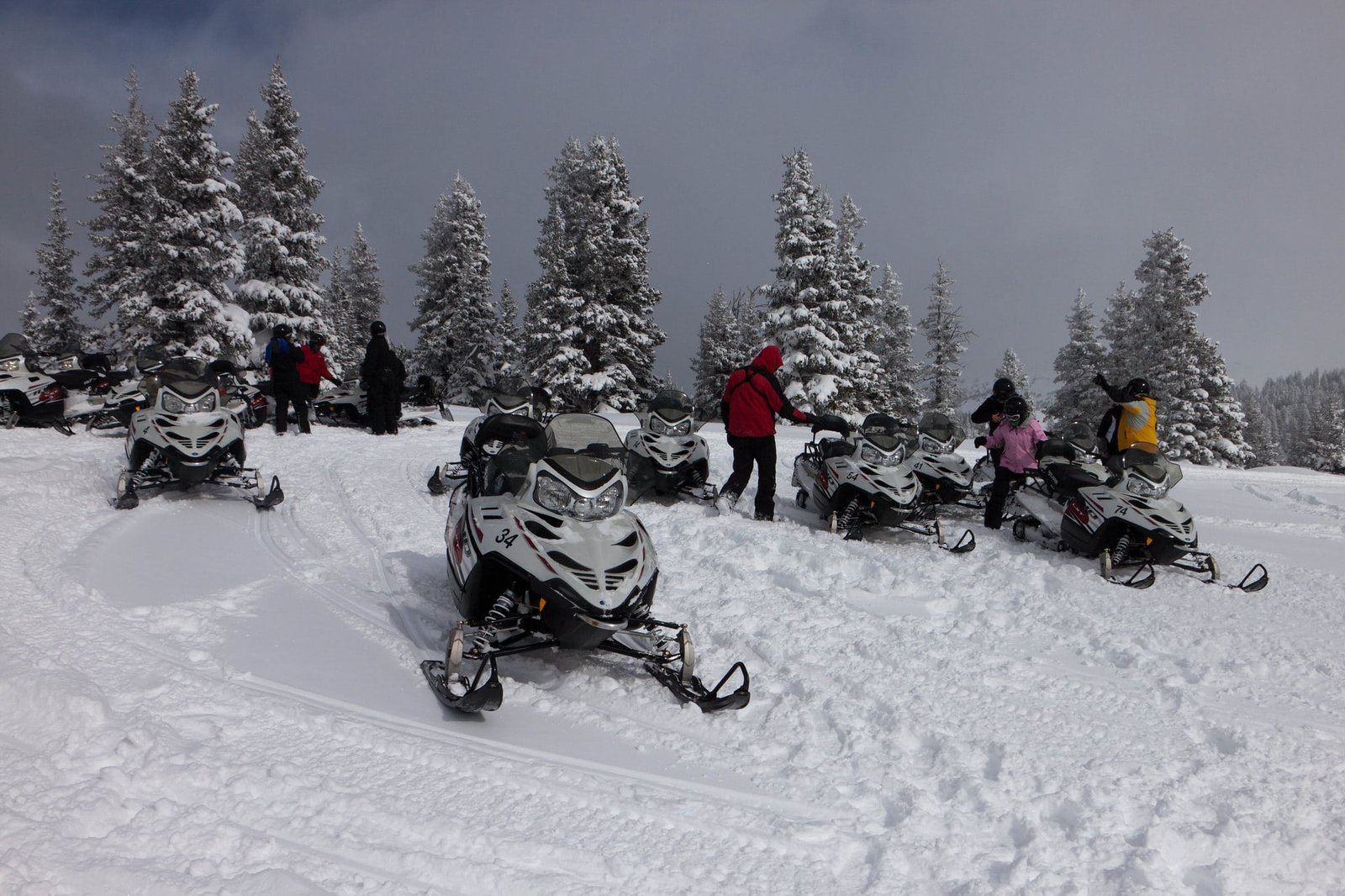 Group of people with snowmobiles in a snow-covered forest during winter, preparing for a ride in gulmarg