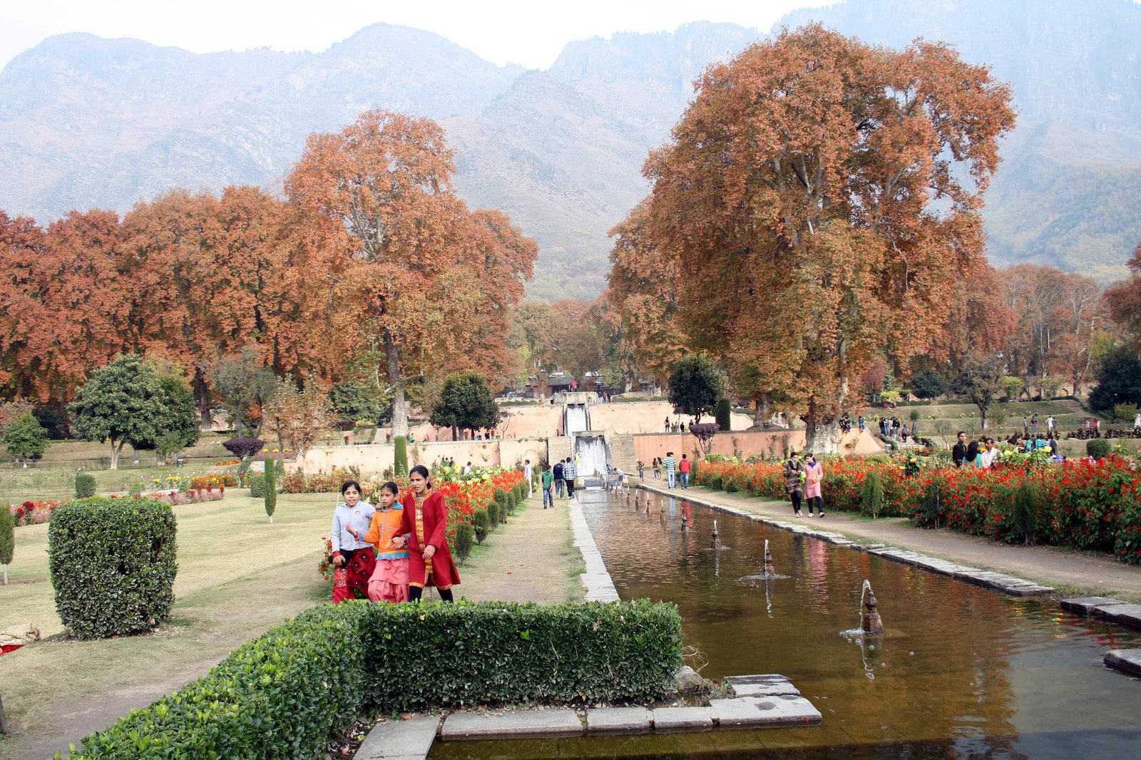 Nishat Bagh in autumn, with vibrant gardens, Chinar trees, and the Zabarwan mountains in the background.