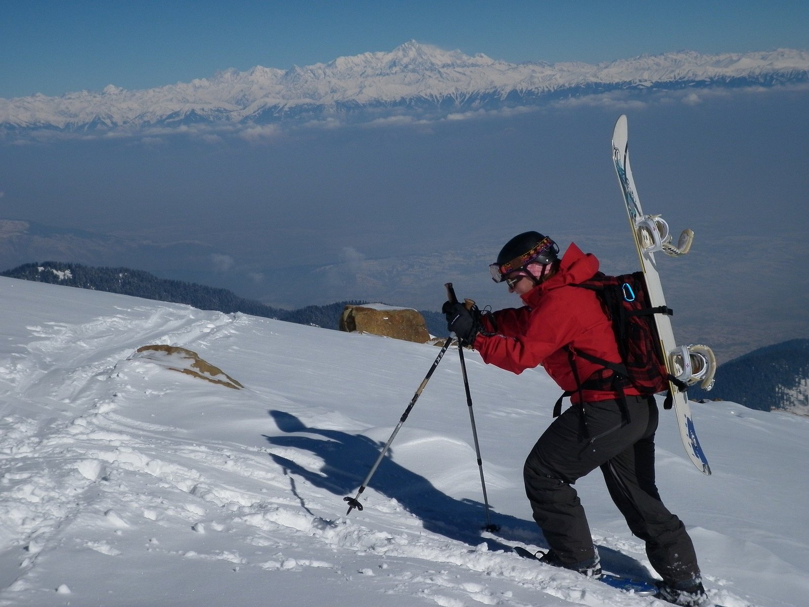 Snowboarder hiking uphill on snowy mountain slope.