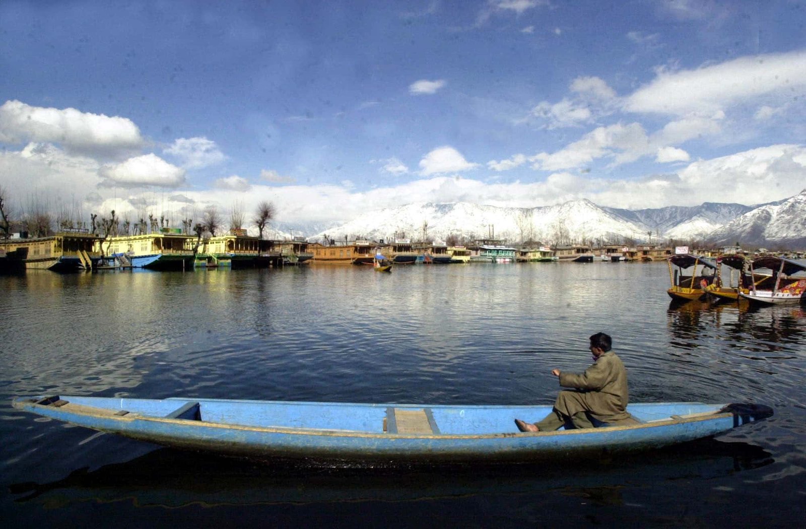 Man rowing a traditional boat on Dal Lake with houseboats in srinagar