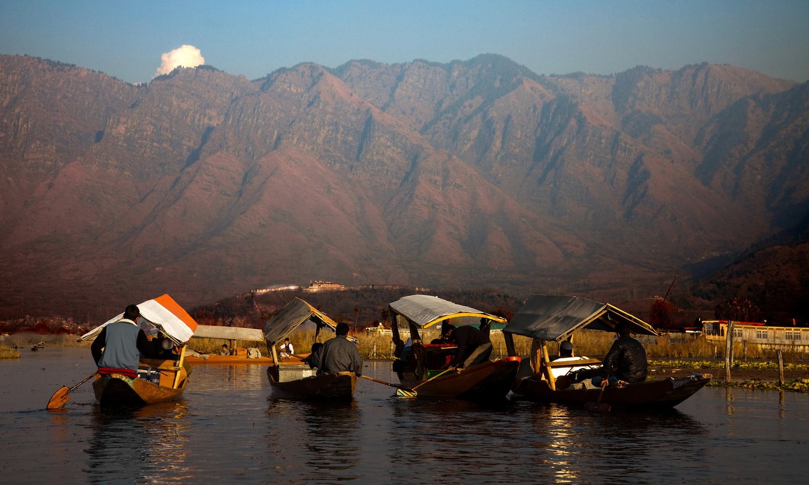 Shikaras on Dal Lake with mountains in the background during golden hour
