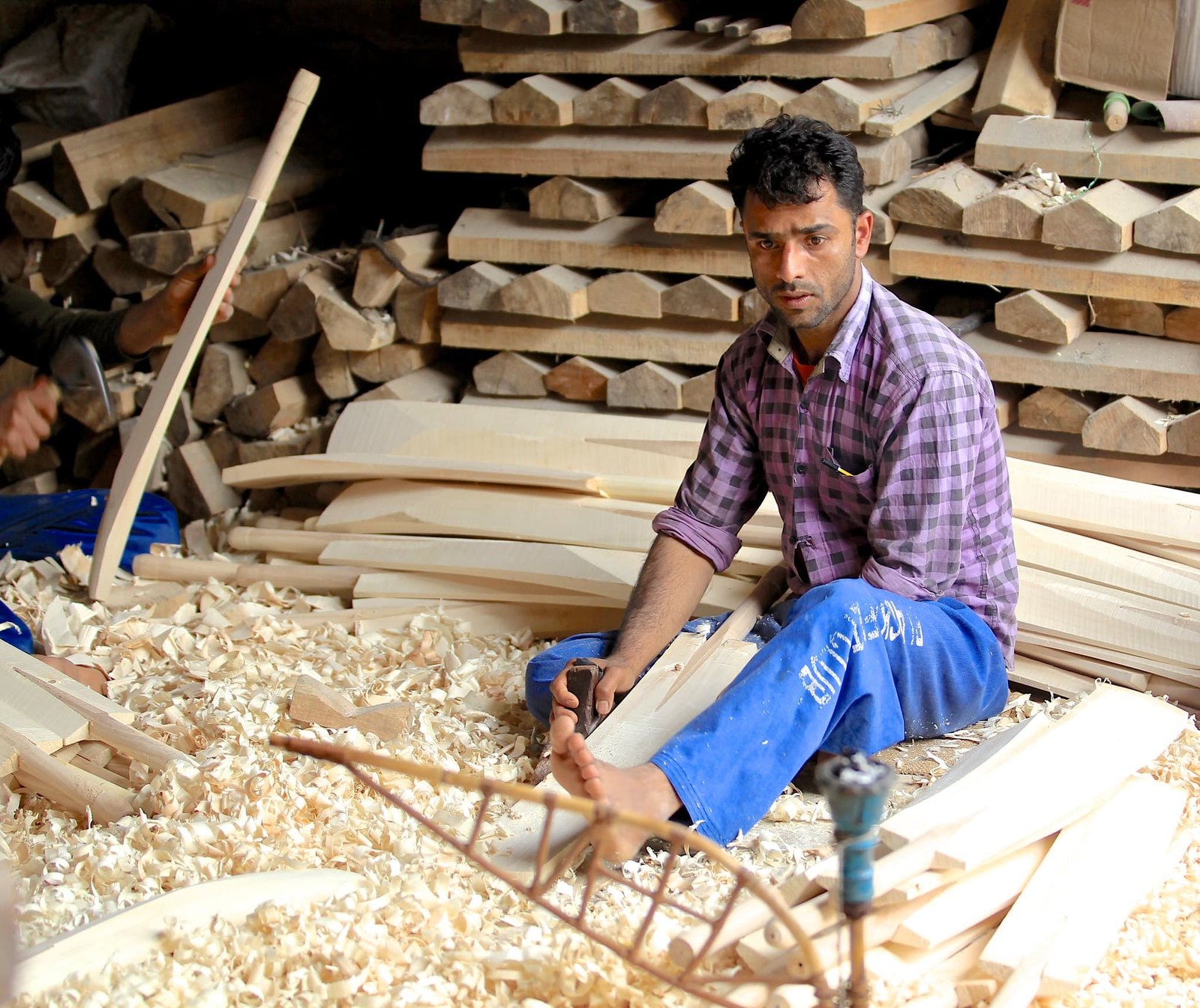 Man making cricket bats in a workshop surrounded by wood shavings
