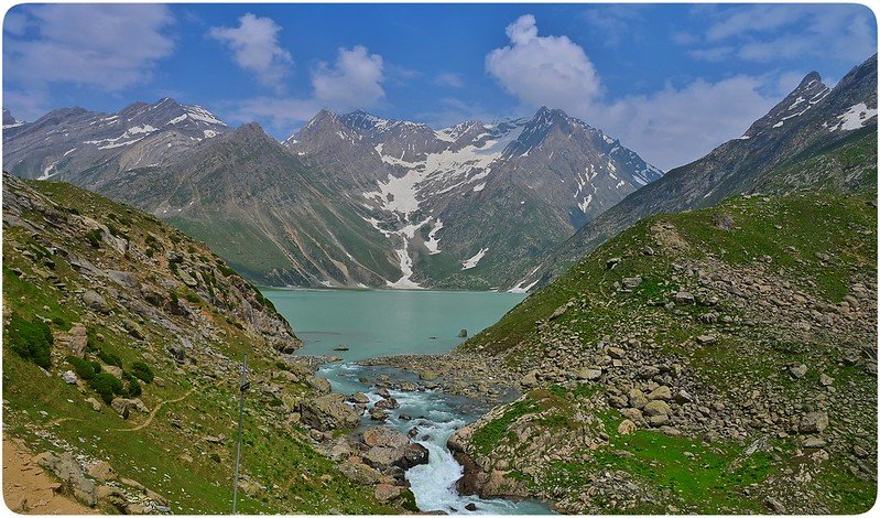 Peaceful lake in Kashmir surrounded by green hills and snowy mountains in summer