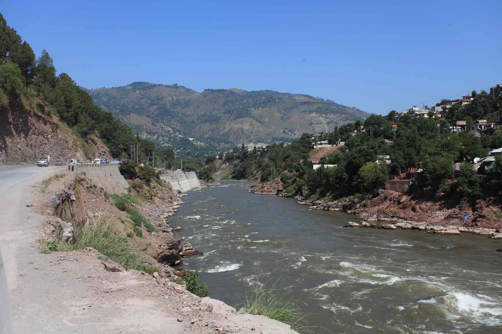 River Jhelum flowing between hills with houses and vehicles