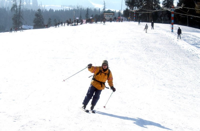 Skier in a yellow jacket skiing downhill on a snowy slope with ski poles