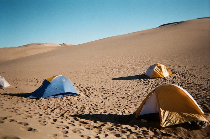 Tents set up on golden sand dunes under a clear blue sky, surrounded by desert landscape