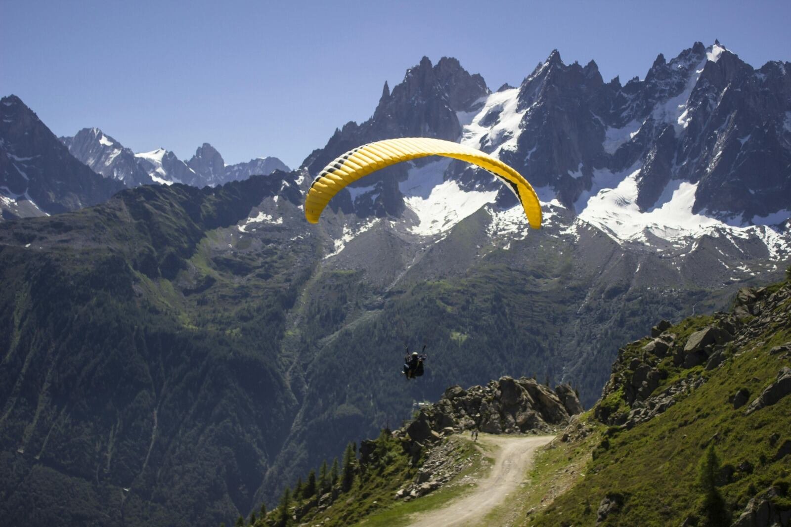 Person paragliding with a yellow canopy over green mountains in ladakh