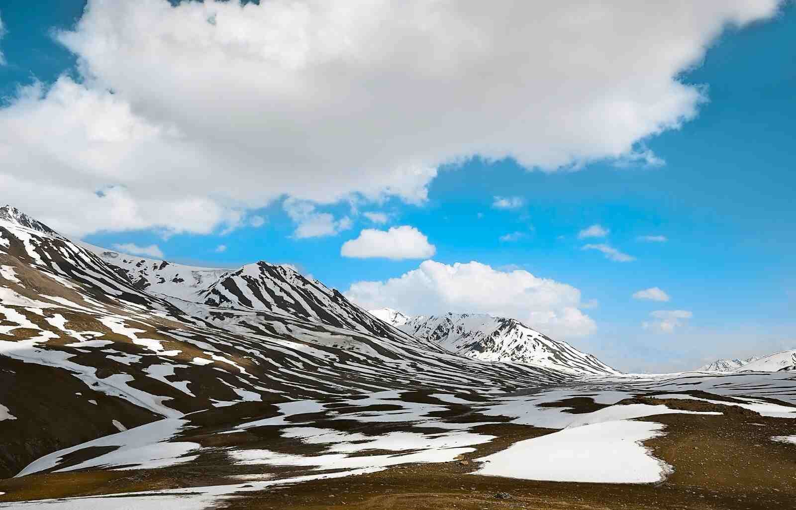 Snow patches scattered over brown mountains under a bright blue sky in Ladakh in february