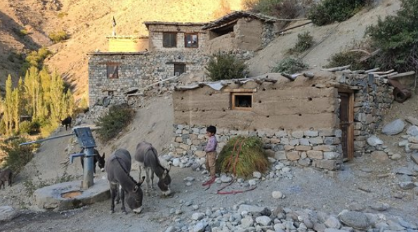 Child with donkeys near mud and stone houses in New Hunderman village