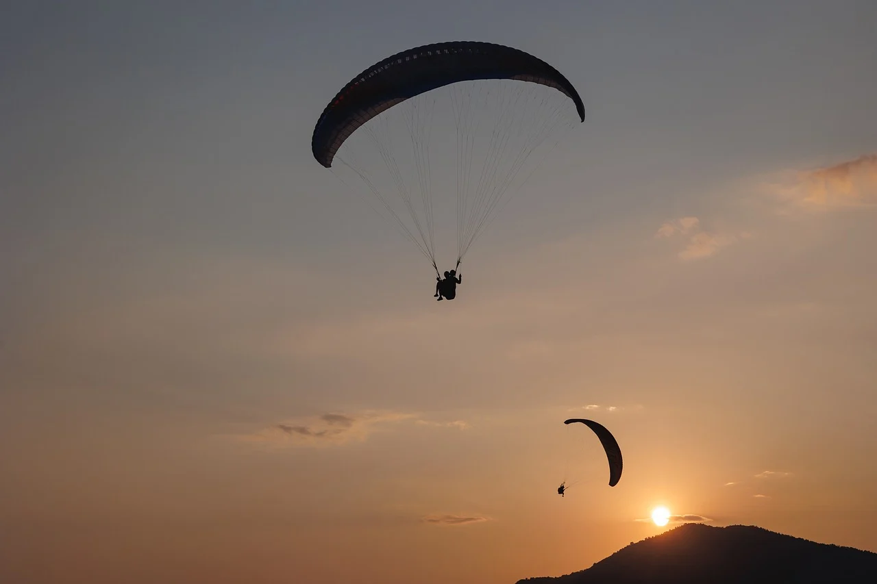 Two paragliders flying at sunset with the sun near a hill in patnitop