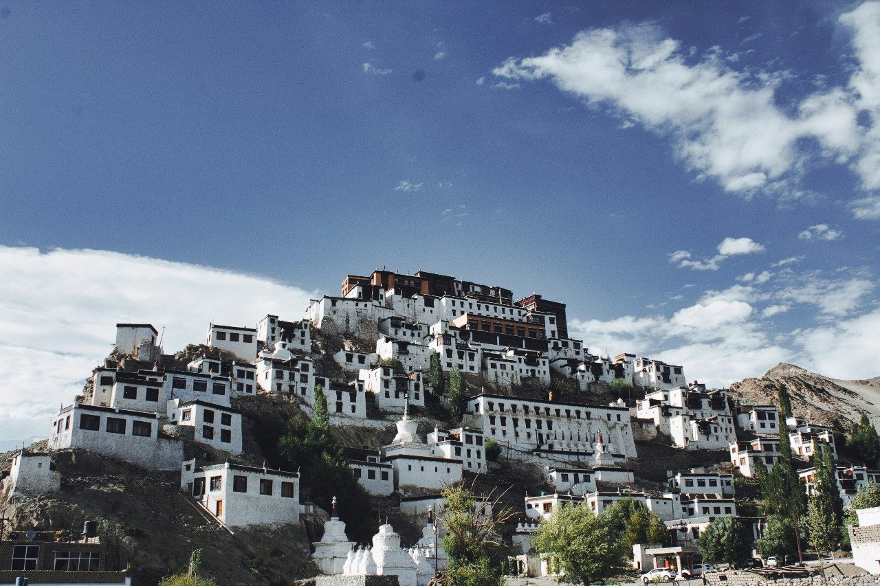 Thiksey Monastery with white buildings stacked on a hill under a blue sky.