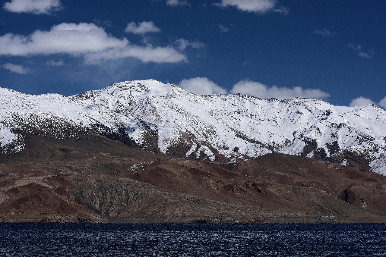 Snow-covered mountains with a lake in front under a clear blue sky