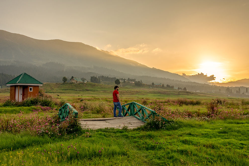 Man enjoying sunset in Gulmarg valley with green fields and mountains