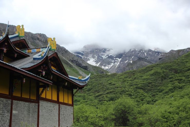 Traditional monastery building with colorful roof near green hills and misty mountains in ladakh