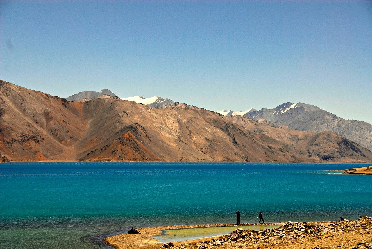 Tourists at Pangong Lake with turquoise water and brown mountains in Ladakh during July